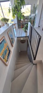 Vue d'un escalier en béton ciré avec un garde-corps noir et des plantes