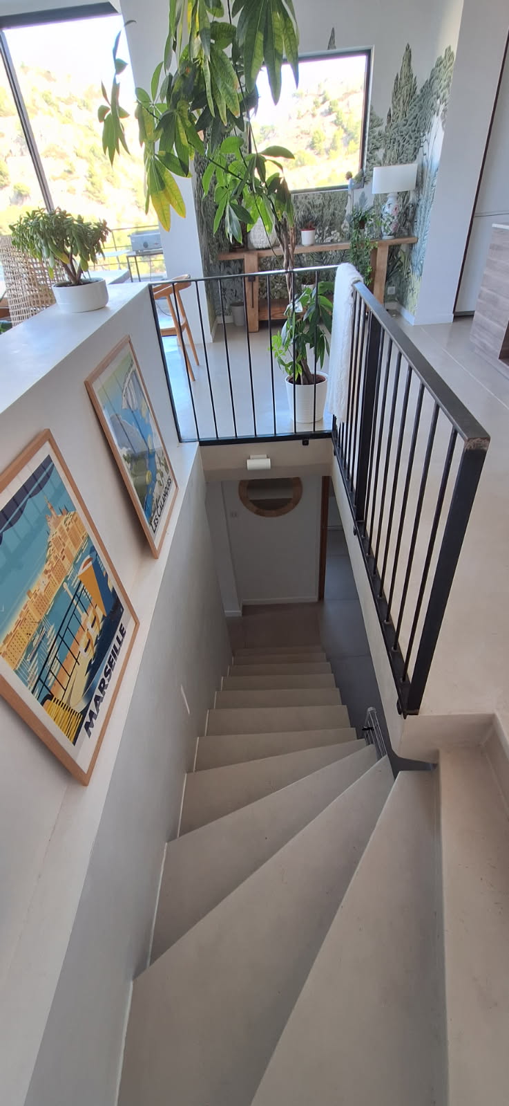 Vue d'un escalier en béton ciré avec un garde-corps noir et des plantes