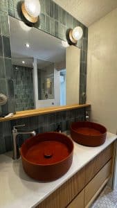 Salle de bain avec deux lavabos ronds en béton ciré orange sur un meuble en bois.