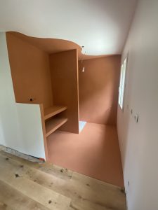 Salle de bain avec mur en béton ciré couleur terracotta en cours de finition