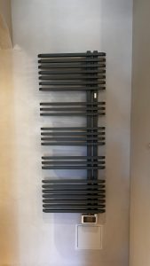 Radiateur sèche-serviettes noir sur un mur en béton ciré