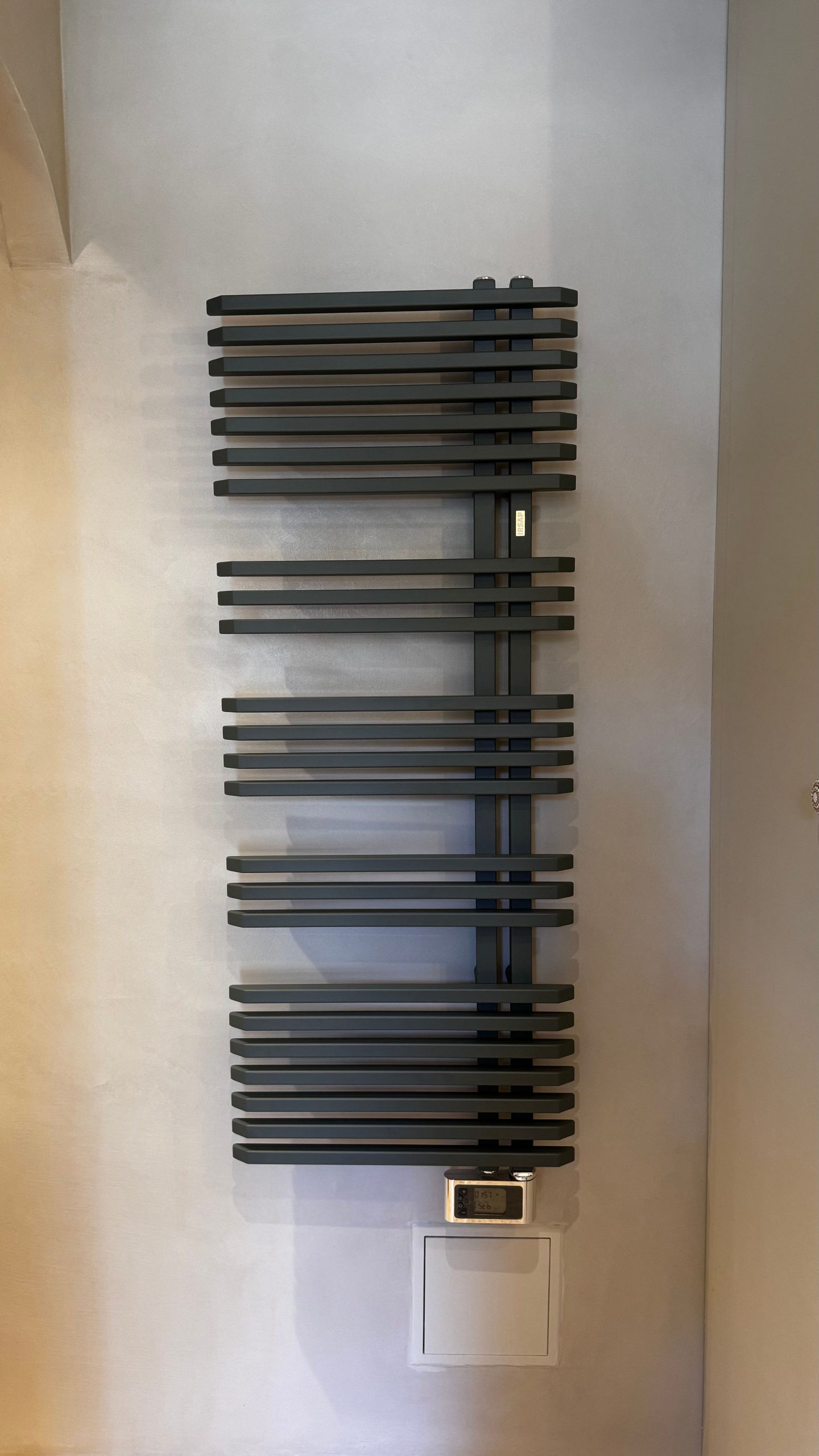 Radiateur sèche-serviettes noir sur un mur en béton ciré