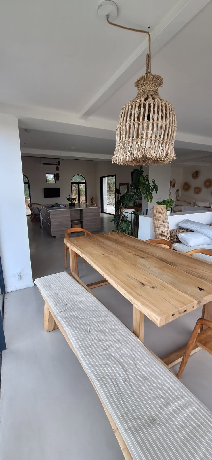 Intérieur d'une salle à manger avec un sol en béton ciré et une suspension en osier.