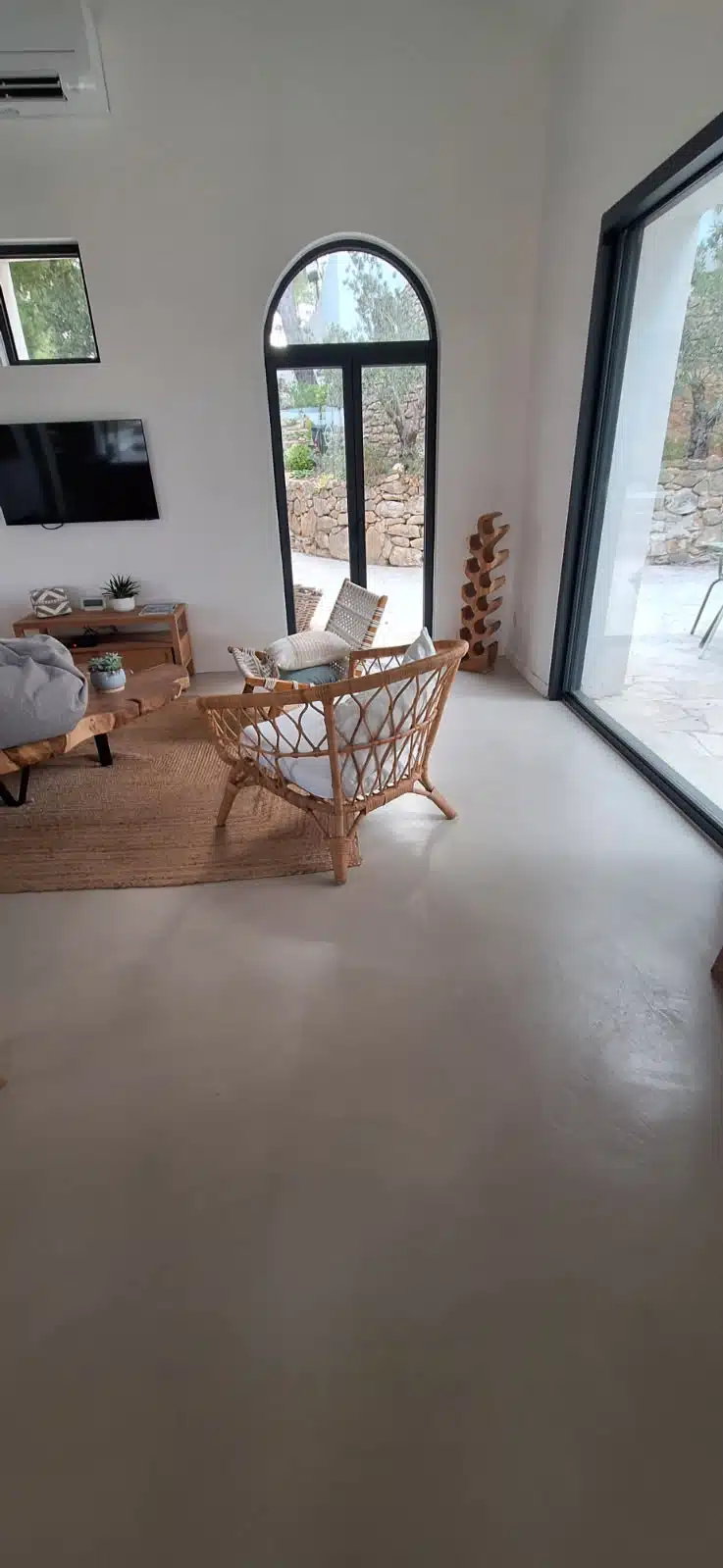 Sol en béton ciré dans un salon lumineux avec fauteuil en rotin.